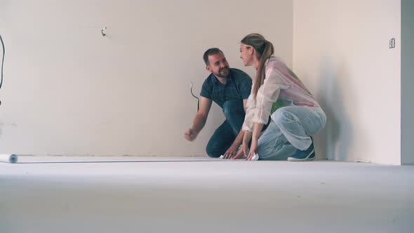 Lovely Couple Unrolls Wallpaper Hugging on Floor in Room alt