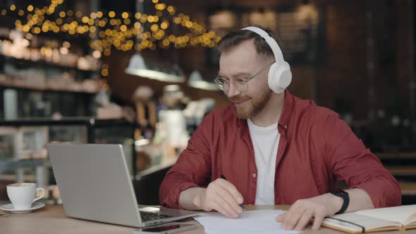 Male Freelancer Sitting at Desk at Cafe and Taking Notes Remotely Studying alt