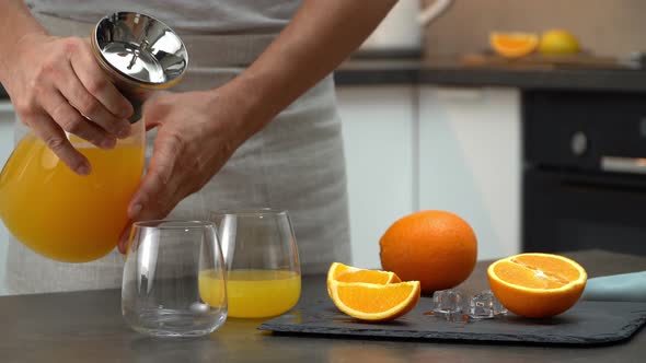 Hands Pour Orange Juice in Glasses From Jug