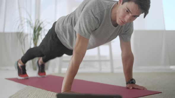 Handsome Young Man in a Gray T-Shirt and Black Shorts Does Sports at Home Online. Attractive Male alt