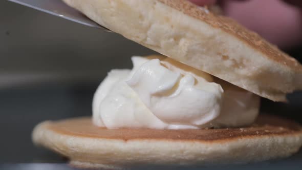 cook puts pancake on stack of tortillas with white cream