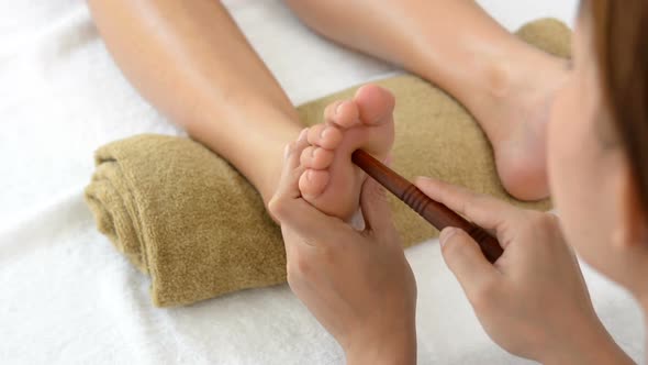 Professional therapist giving traditional thai foot massage with stick to a woman in spa