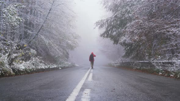 Happy Man Walking on Frozen Asphalt Road Carrying His Backpack in Winter Conditions alt