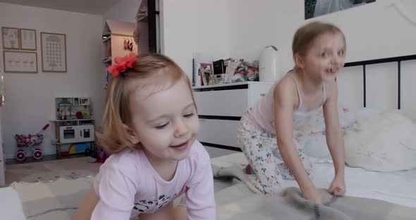 Two Little Girls are Playing at Home Jumping for Joy and Smiling Nicely alt