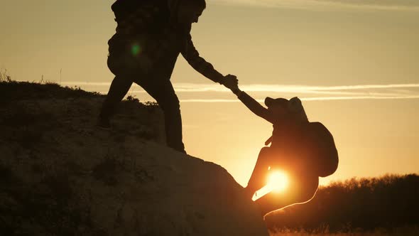 Silhouette of Helping Hand Between Two Climber. Two Hikers on Top of the Mountain alt
