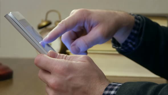 Male's Hand Holding Digital Tablet with Book Stack on the Desk alt