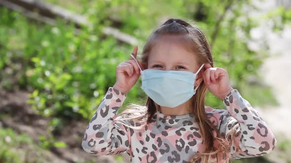 Portrait of little girl takes off a protective face mask standing outdoor.