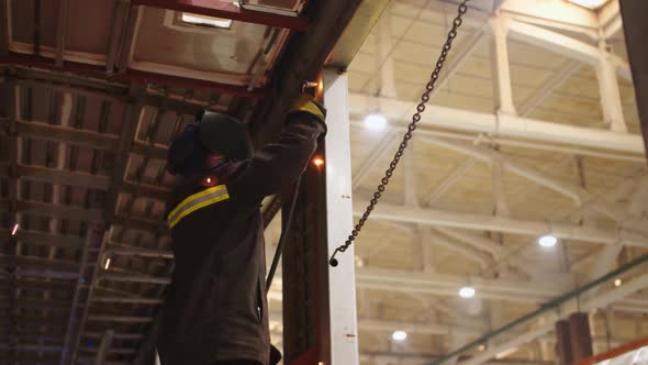 Closeup View From the Bottom to Factory Laborer in Protective Suit and Safety Mask Using a Welding