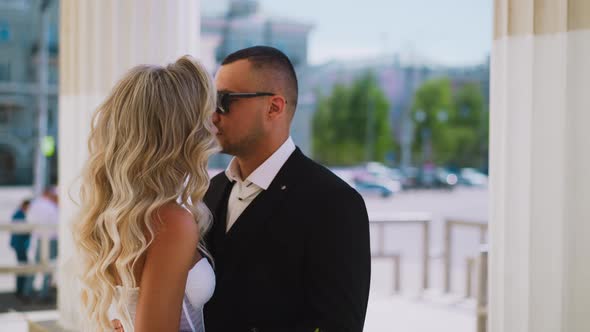Man with Sunglasses Hugs Beloved Wife with Hairdo By Columns alt