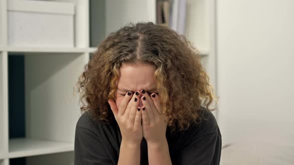 Teenage Girl Sits Alone and Cries Covering Her Face with Her Hands alt