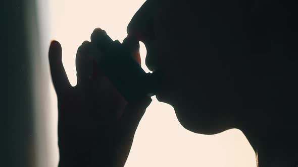 Person Silhouette Using Inhaler for Breathe Disease Closeup alt