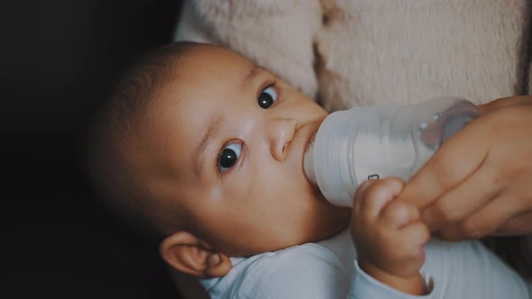 Close Up Adorable Dark Skin Baby Drinking His Milk From the Bottle in Mothers Hands alt