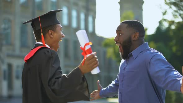 Excited Dad and Graduating Son Hugging Outdoors, Study Achievement, Education alt