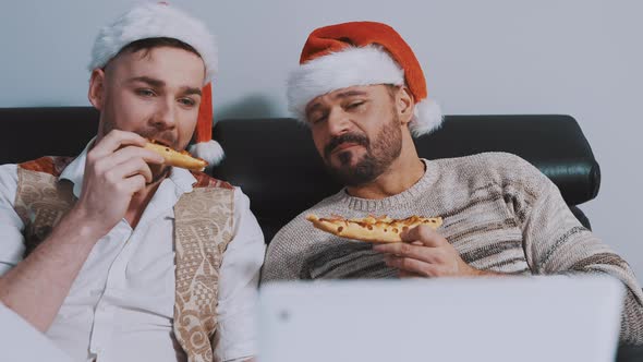 Lovely Gay Male Couple with Christmas Hats Eating Pizza and Watching Movies on the Christmas Eve alt