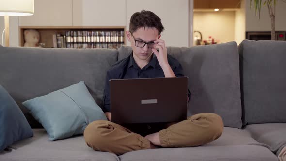 A Young Guy with Glasses Sits on a Sofa with a Laptop alt