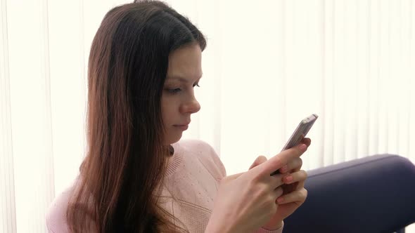 Young Woman Brunette Is Typing a Message on Her Mobile Phone and Looking at Screen