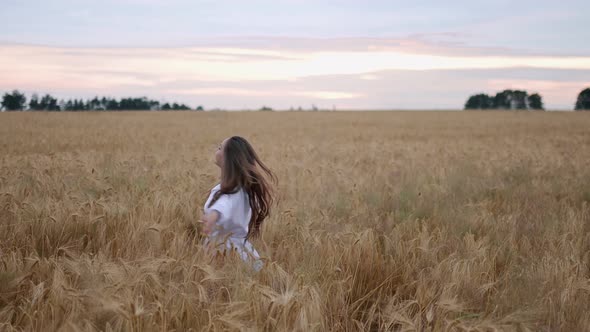 A Young Girl Happily Walking in Slow Motion Through a Field Touching with Hand Wheat Ears Beautiful