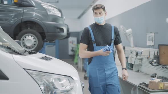 Young Confident Auto Mechanic in Covid Face Mask Walking in Auto Repair Shop To Tools Set alt
