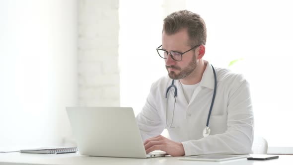 Doctor Showing Thumbs Up Sign While Using Laptop in Office alt