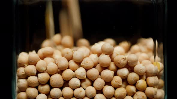 Closeup of Falling Down Chickpeas Into Glass Jar on Black Background alt