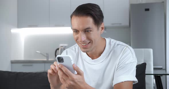 Happy Businessman Enjoying Success on Mobile Phone Sitting on Sofa at Home alt