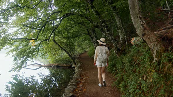 Young woman in a hat walking along the path along the lake. Plitvice Lakes alt