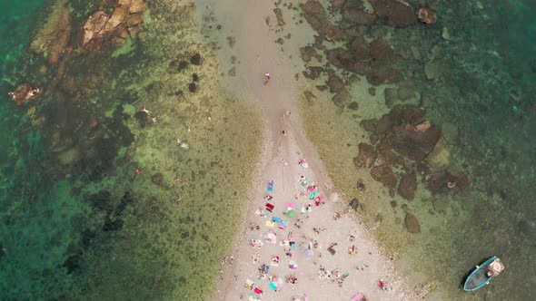 Top down aerial view of a sand bridge connecting two beaches, surrounded by a shallow sea with a cle alt