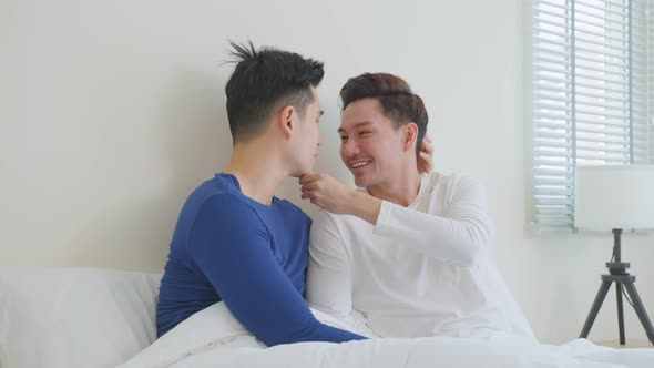 Asian handsome male gay couple sitting on bed and look at each other. alt