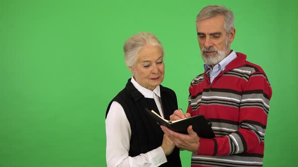 An Elderly Couple Writes Something Into a Notebook - Green Screen Studio alt