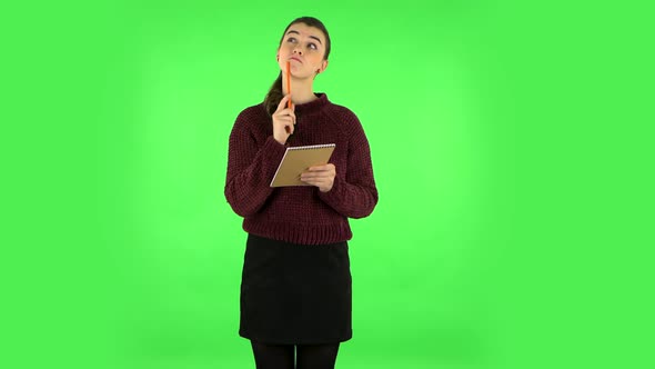 Girl Stands and Thinks, Then Writes with Pencil in Notebook. Green Screen alt