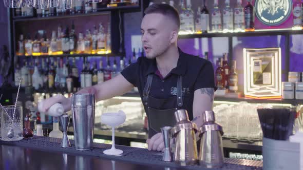 Cute Professional Barman Pouring Drink From Measuring Cup Into a Metal Shaker alt