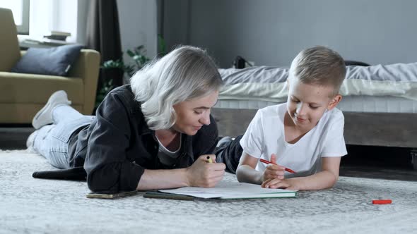 A Young Mother and A Baby Boy Are Sitting on the Floor, The Mother Is Teaching the Child To Draw alt