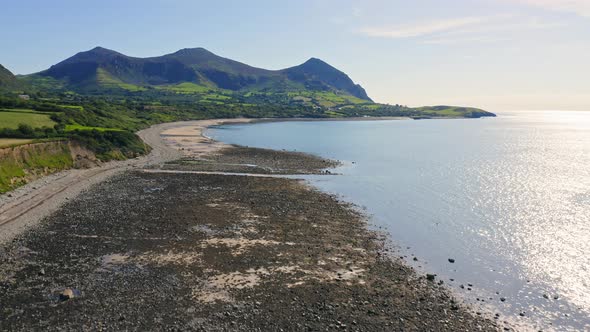 Drone flying over Trefor Beach and rugged Welsh coast in Wales with Yr Eifl Mountains in background  alt