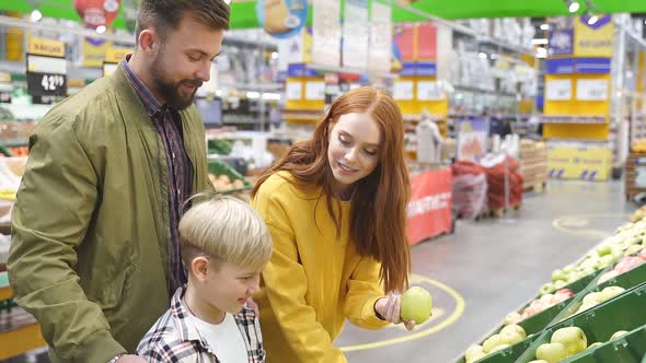 Young Happy Family Chooses Fresh Apples Standing in the Supermarket