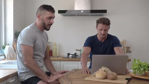 Handsome gay male couple disagreeing and arguing in kitchen at home