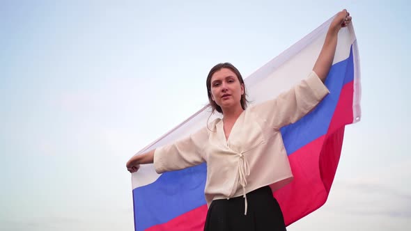 Portrait of a Beautiful Russian Woman with a Flag at Sunset Against the Sky