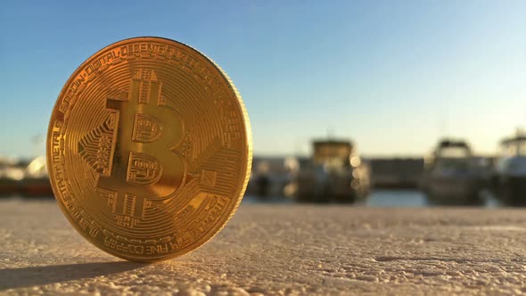 Golden Bitcoin Close Up On Wall In Harbor With Boats At Background