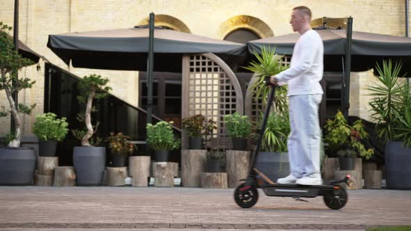 Side View Man on Escooter Passing Right to Left on Town Street in Slow Motion alt