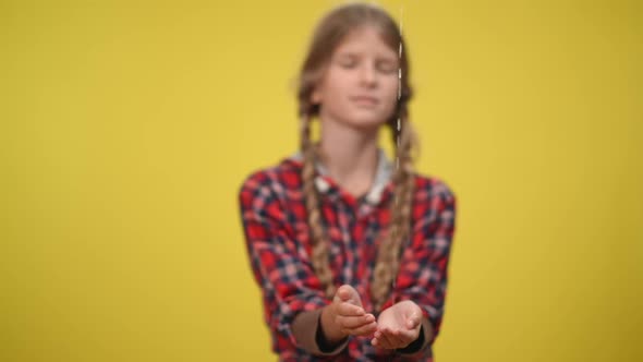 Water Pouring in Slow Motion on Hands of Blurred Teenage Caucasian Girl at Yellow Background alt