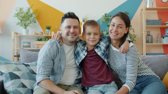 Portrait of Parents and Child Smiling Embracing on Sofa in Modern Studio Apartment alt
