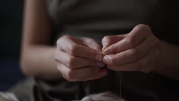 Close-up view of female hands inserting a thread into a needle hole for sewing. Handmade needlework. alt