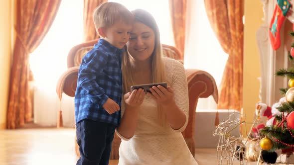 Footage of Little Smiling Boy with Young Mother Watching Family Photographs on Smartphone While