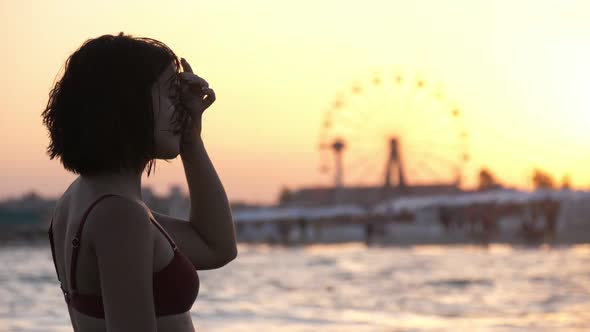 Cheery Girl in Bikini Putting Her Hair in Order on a City Beach at Striking Sunset in Slow Motion