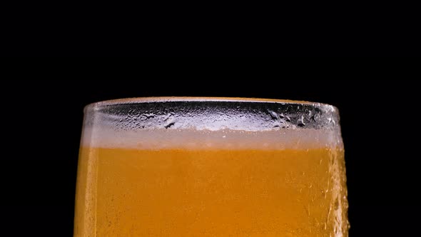 Beer with Bubbles and Foam in a Glass on Black Background
