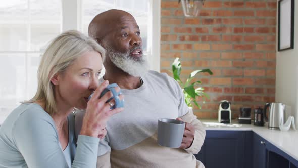 Mixed race senior couple drinking coffee together in the kitchen at home alt