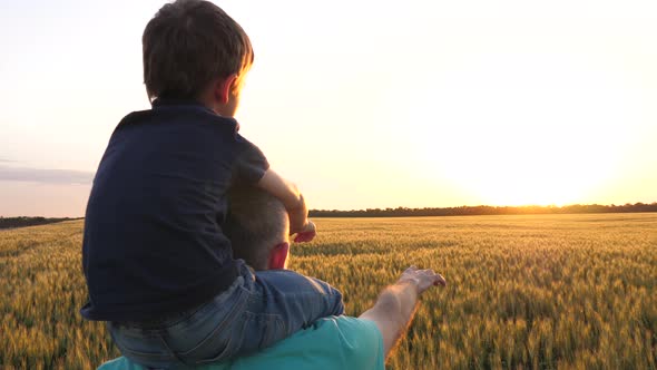 The Boy Is Sitting on His Father's Neck. Father and Son Point To the Horizon at Sunset. Happy Family alt