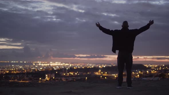 Man with Outstretched Arms Looking at City View at Sunset alt