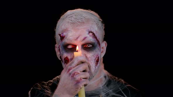 Man with Halloween Zombie Bloody Wounded Makeup Trying to Scare Spells Conjures Over a Candle alt
