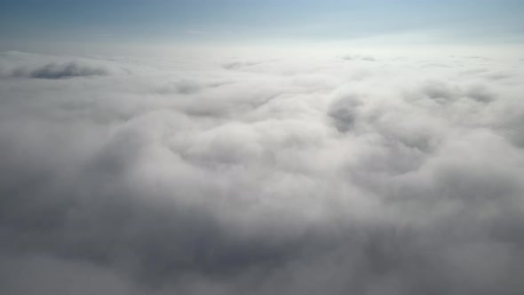Aerial shot of flying over a layer of soft clouds at dawn alt
