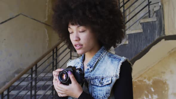 African american woman taking pictures with digital camera while standing near stairs alt